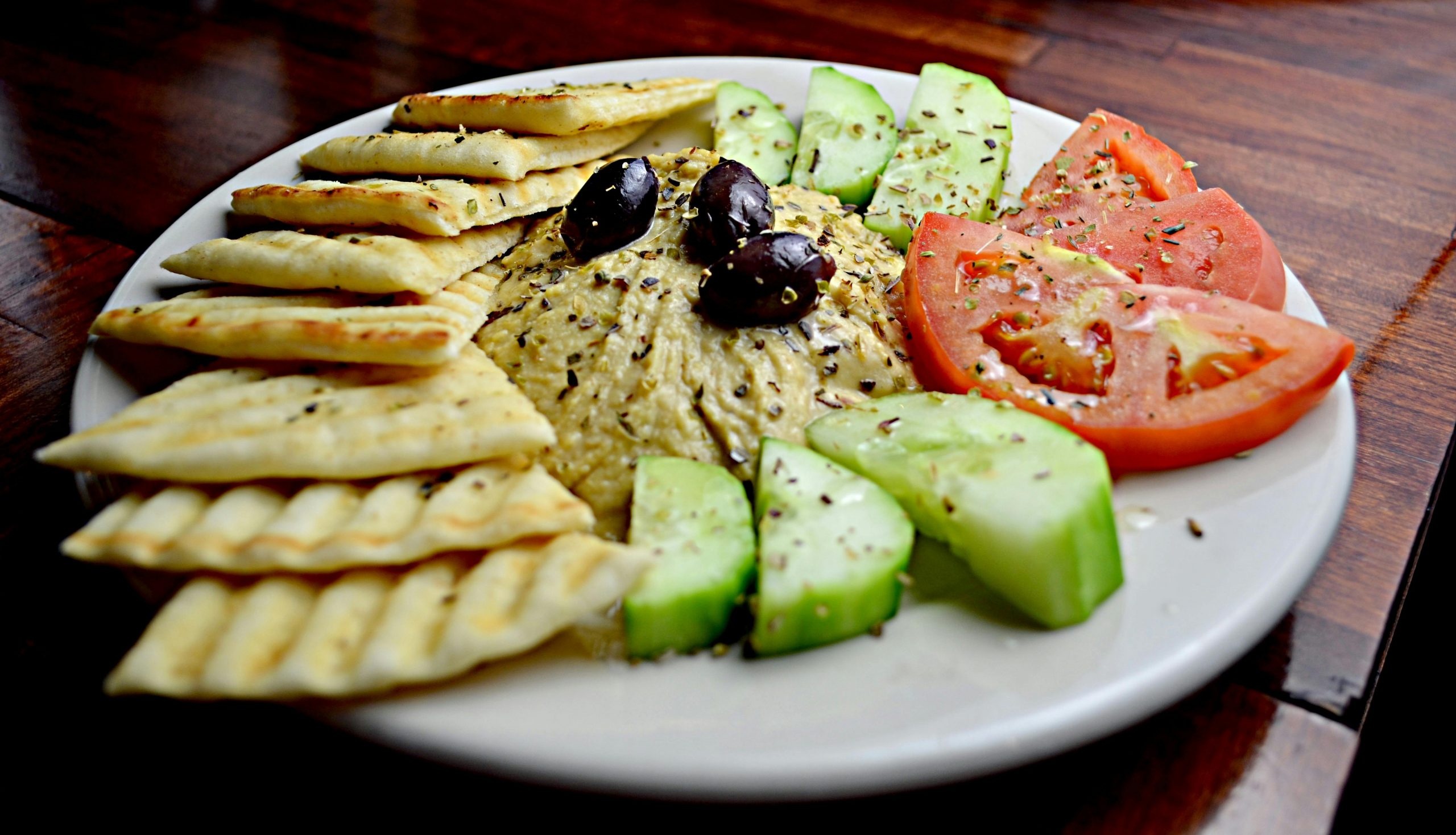 Home Delicious Mediterranean platter featuring hummus, pita, cucumbers, tomatoes, and olives.